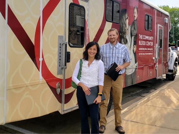 Two FTI team members standing by the Community Blood Center's bus