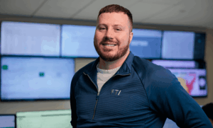 FTI team member smiling in front of screens in the Network Operations Center