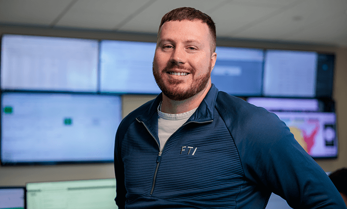 FTI team member smiling in front of screens in the Network Operations Center